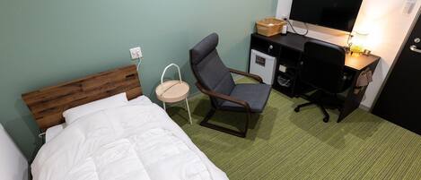 A hotel room with a bed, a desk, a chair, a television, and a small refrigerator.