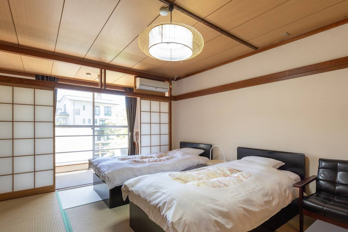 A traditional Japanese-style room with tatami flooring, two beds, a black leather sofa, and a shoji screen door.