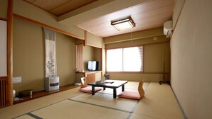 Ein traditioneller japanischer Raum mit Tatami-Böden, einem niedrigen Tisch mit Kissen, einem Fernseher und einer Heizung.