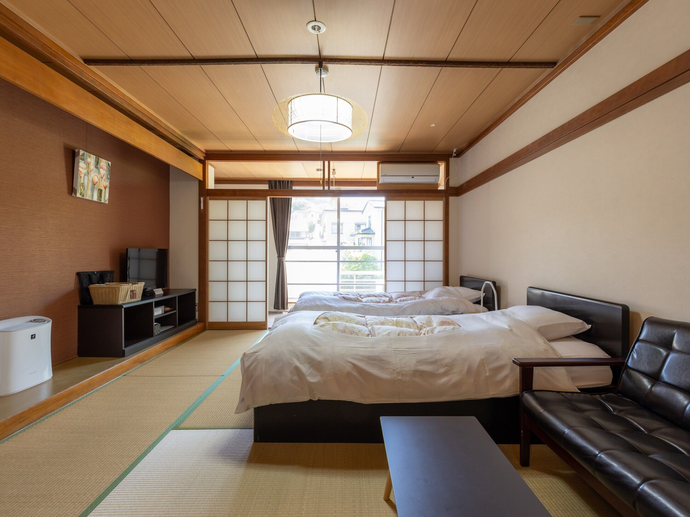 A traditional Japanese-style bedroom with tatami flooring, a futon bed, a low wooden bench, and a sliding shoji screen door.