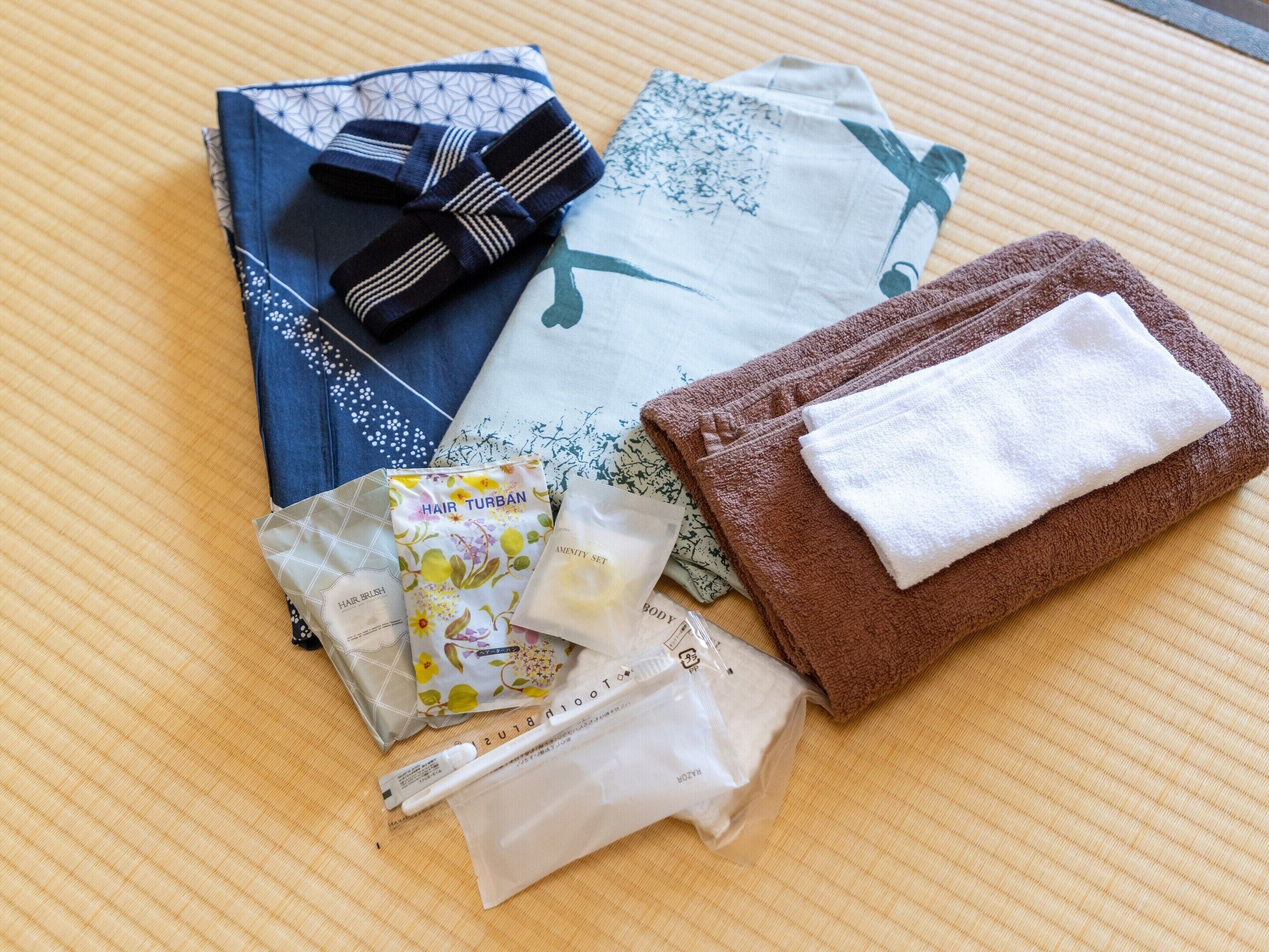 A neatly arranged set of personal care items including a hairbrush, hair turban, towels, and toiletries on a textured surface.