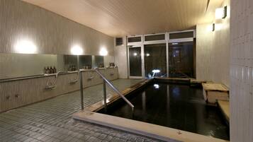 A modern indoor swimming pool with tiled floors, a wooden deck, and a glass wall.