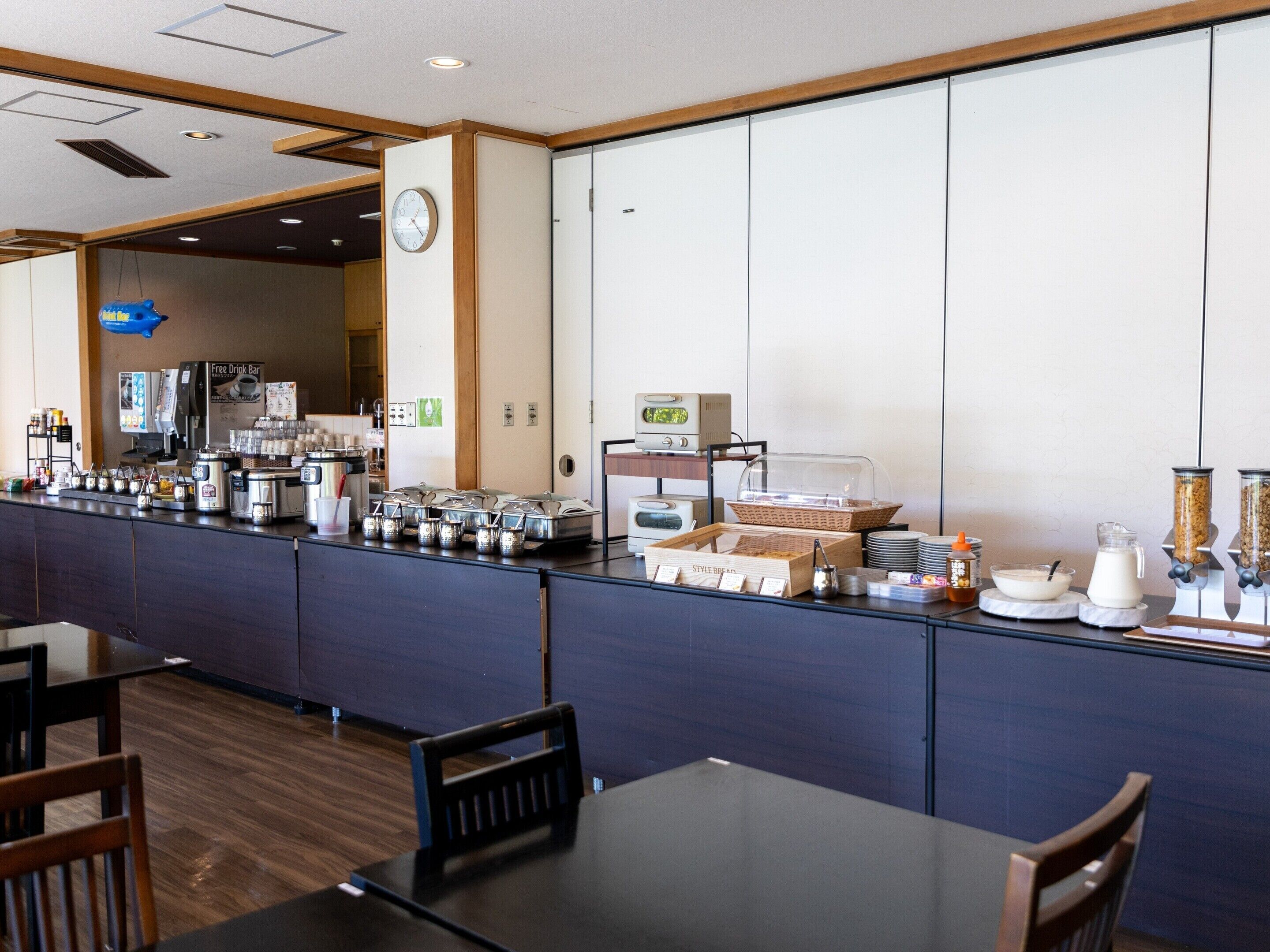 En morgenmadsbuffet med forskellige spisemuligheder, herunder en kaffemaskine, müsli og en juiceautomat.