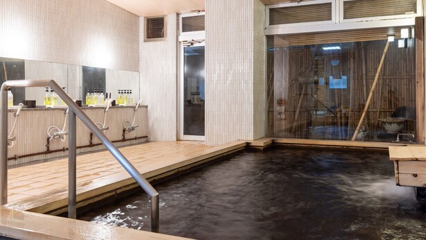 Ein traditionelles japanisches Onsen mit Holzterrasse, kleinem Becken und einem durch Glas geschützten Bereich mit einem Bambusbesen.