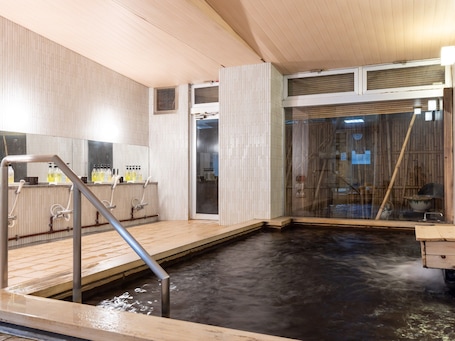 A traditional Japanese onsen with a wooden deck, a small pool, and a glass-enclosed area with a bamboo rake.
