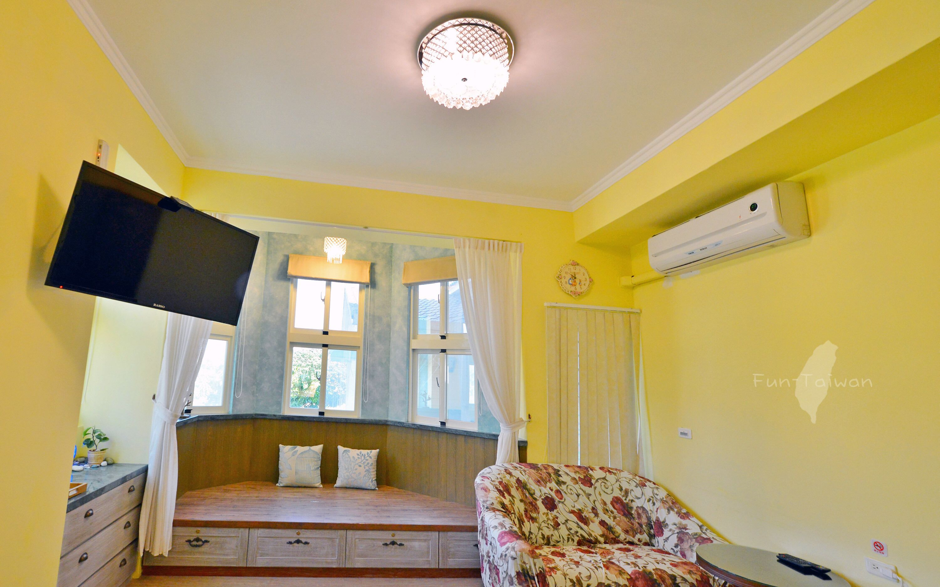 Una habitación con una cama, una silla, un televisor montado en la pared y una ventana con cortinas.