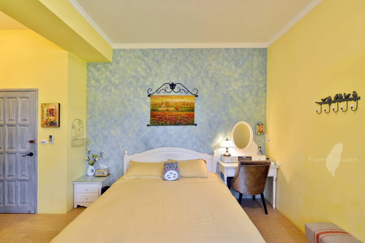 Quarto com cama, mesa de cabeceira, cadeira e luminária na parede.