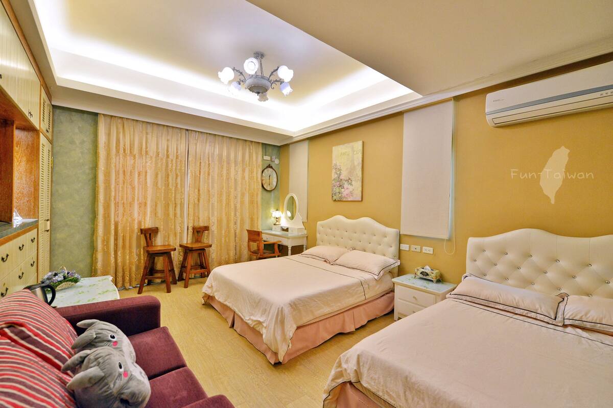 Quarto de hotel com duas camas, uma escrivaninha com candeeiro, uma cadeira, televisão e um mapa na parede.