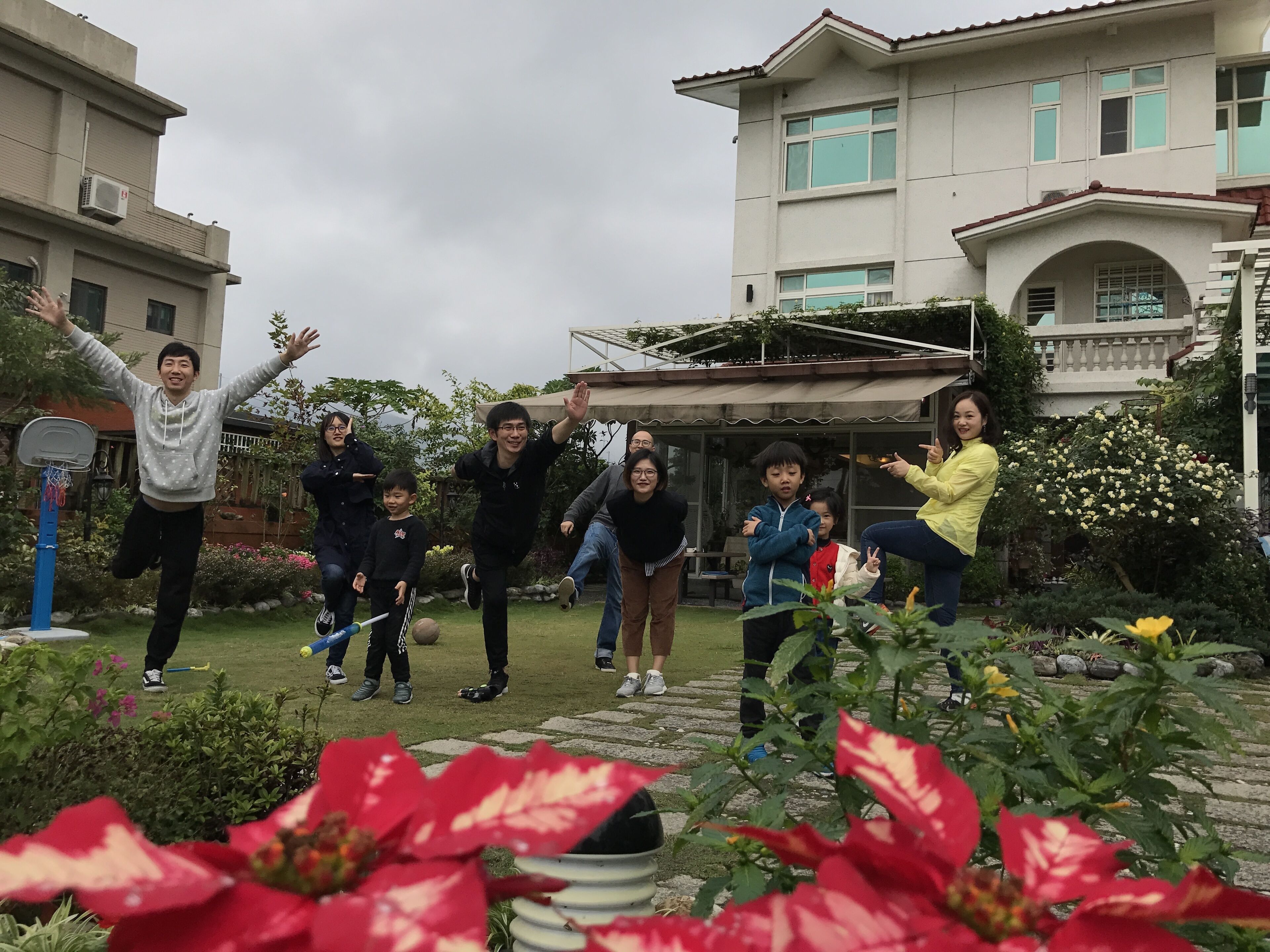 A group of people in a garden with a basketball hoop, a covered patio, and a building in the background.