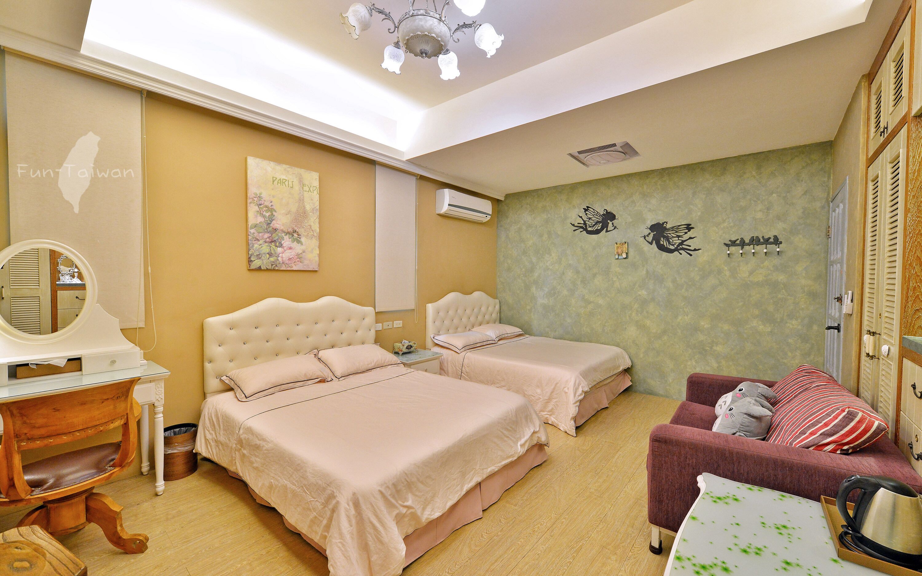 A hotel room with two beds, a vanity with a mirror, a desk, a chair, and a small table.