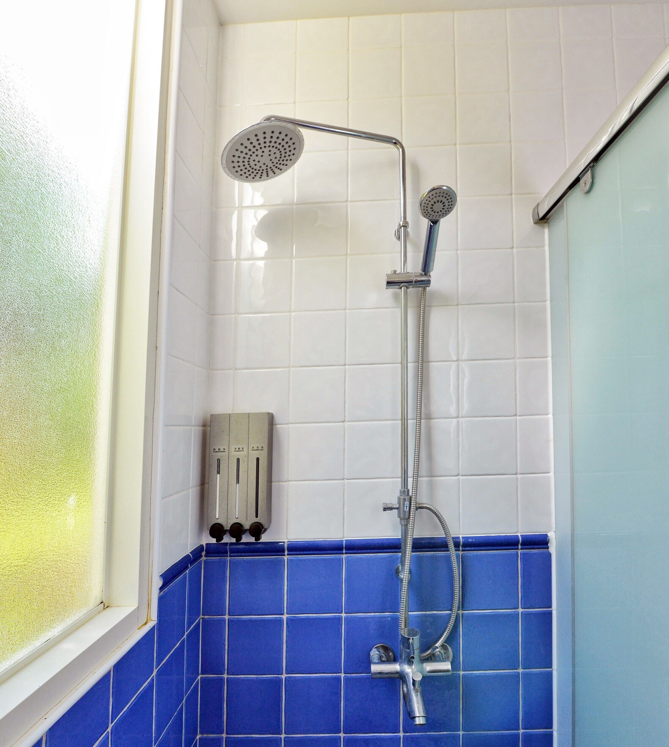 A shower with a handheld showerhead and a wall-mounted faucet, a control panel with multiple settings, and a window with frosted glass.