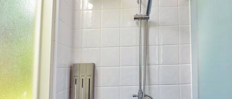 A shower with a handheld showerhead and a wall-mounted faucet, a control panel with multiple settings, and a window with frosted glass.