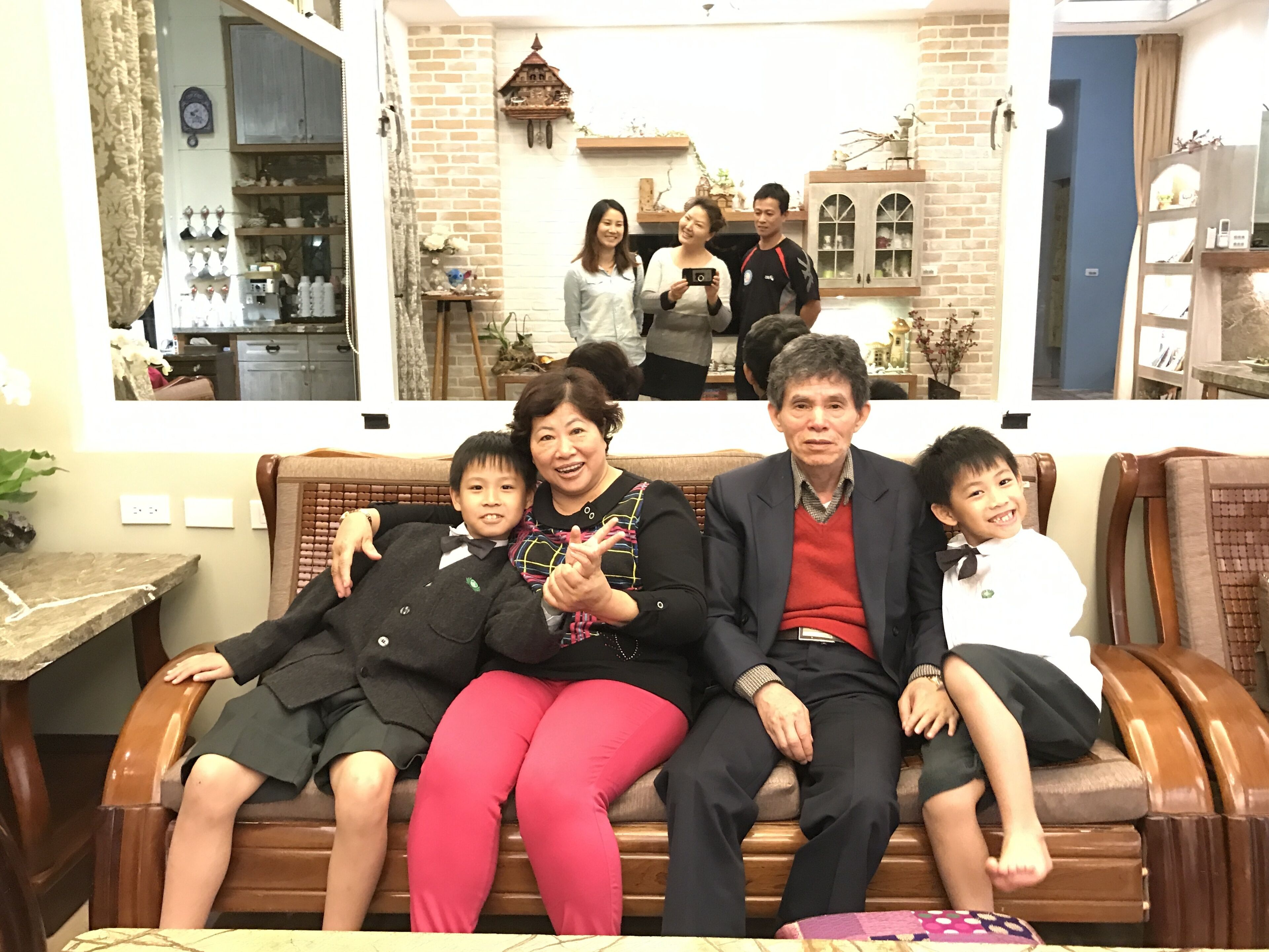 A family sitting on a wooden bench in a cozy room with brick walls, a wooden table, and a mirror.