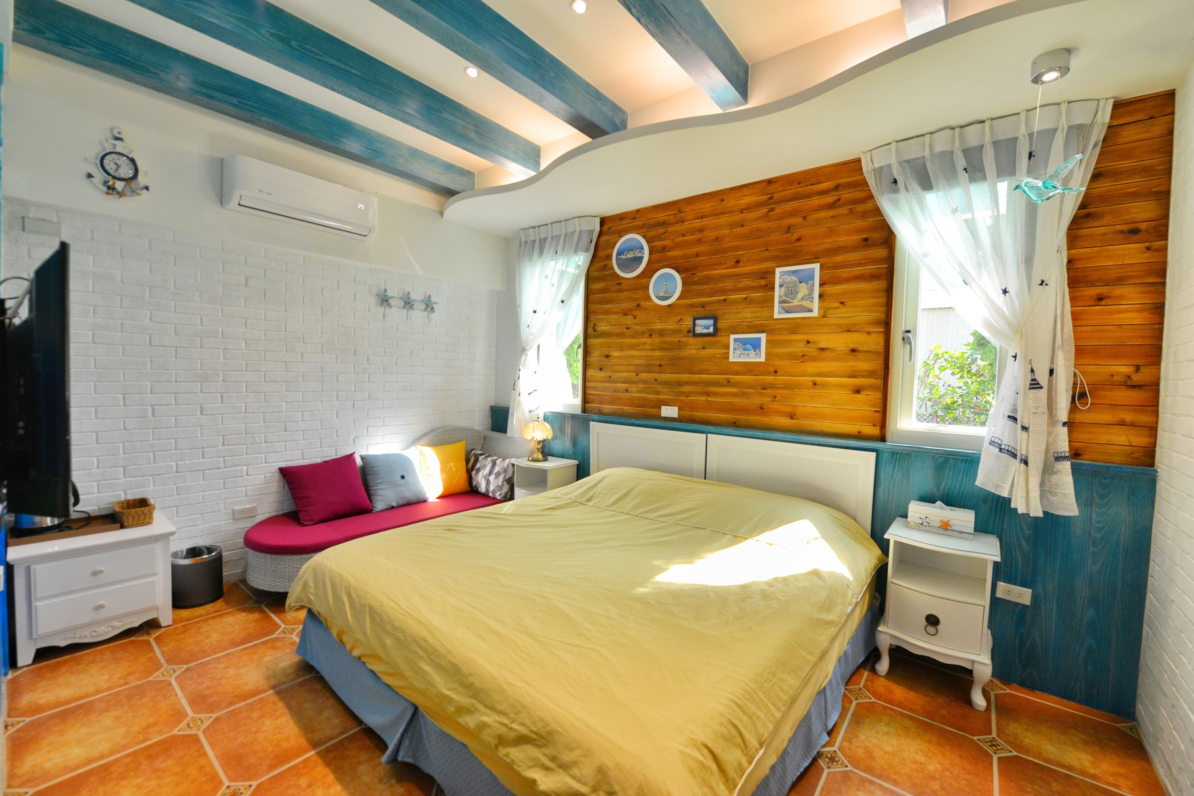 Un dormitorio con cama, mesita de noche, televisor y ventana con cortinas.