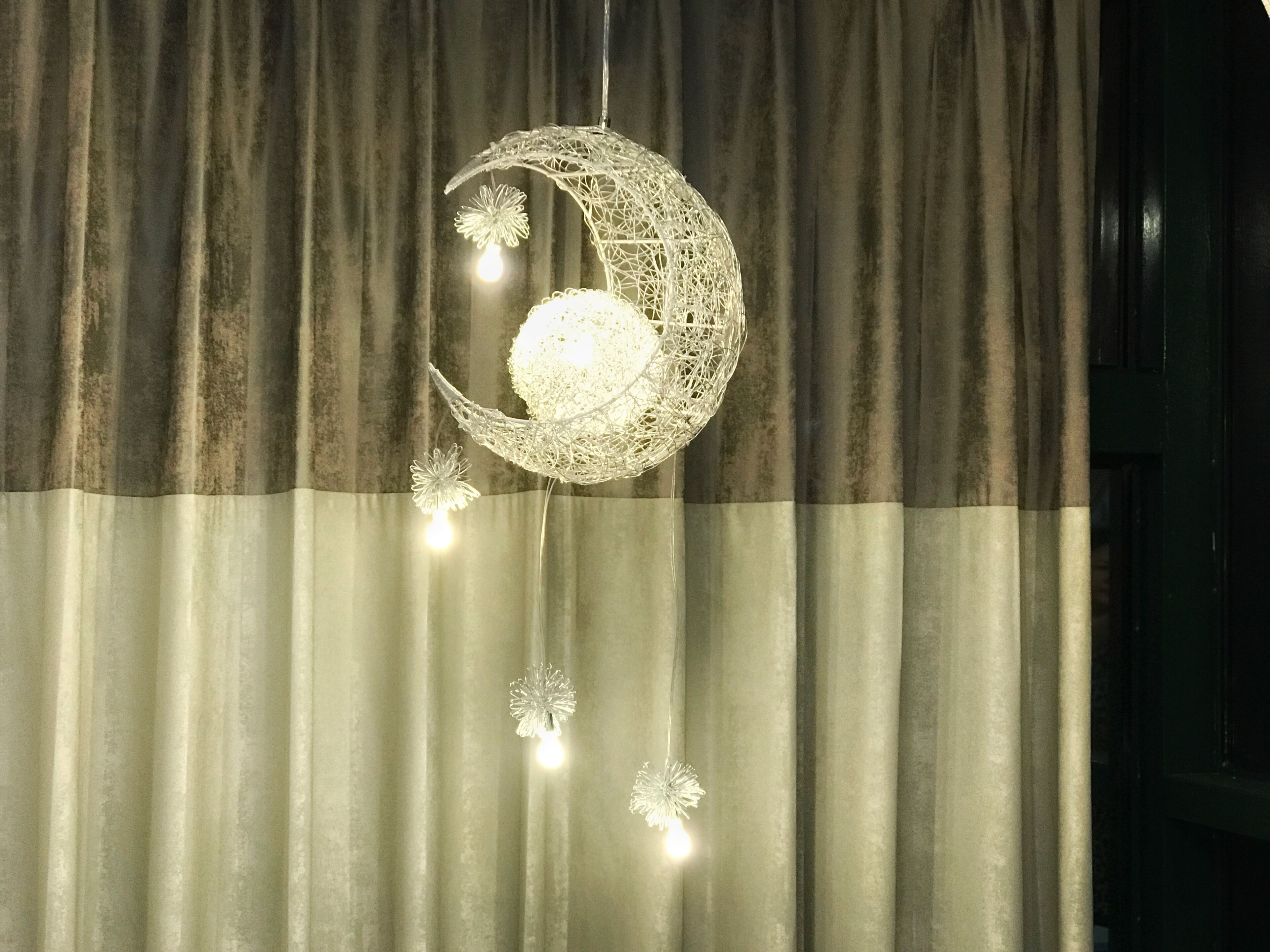 A decorative moon-shaped hanging light fixture with a spherical light bulb in the center, suspended from a curtain.