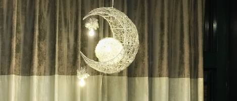 A decorative moon-shaped hanging light fixture with a spherical light bulb in the center, suspended from a curtain.