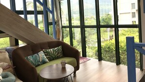 Una habitación con sofá, una mesita redonda y vistas a zonas verdes a través de amplios ventanales.