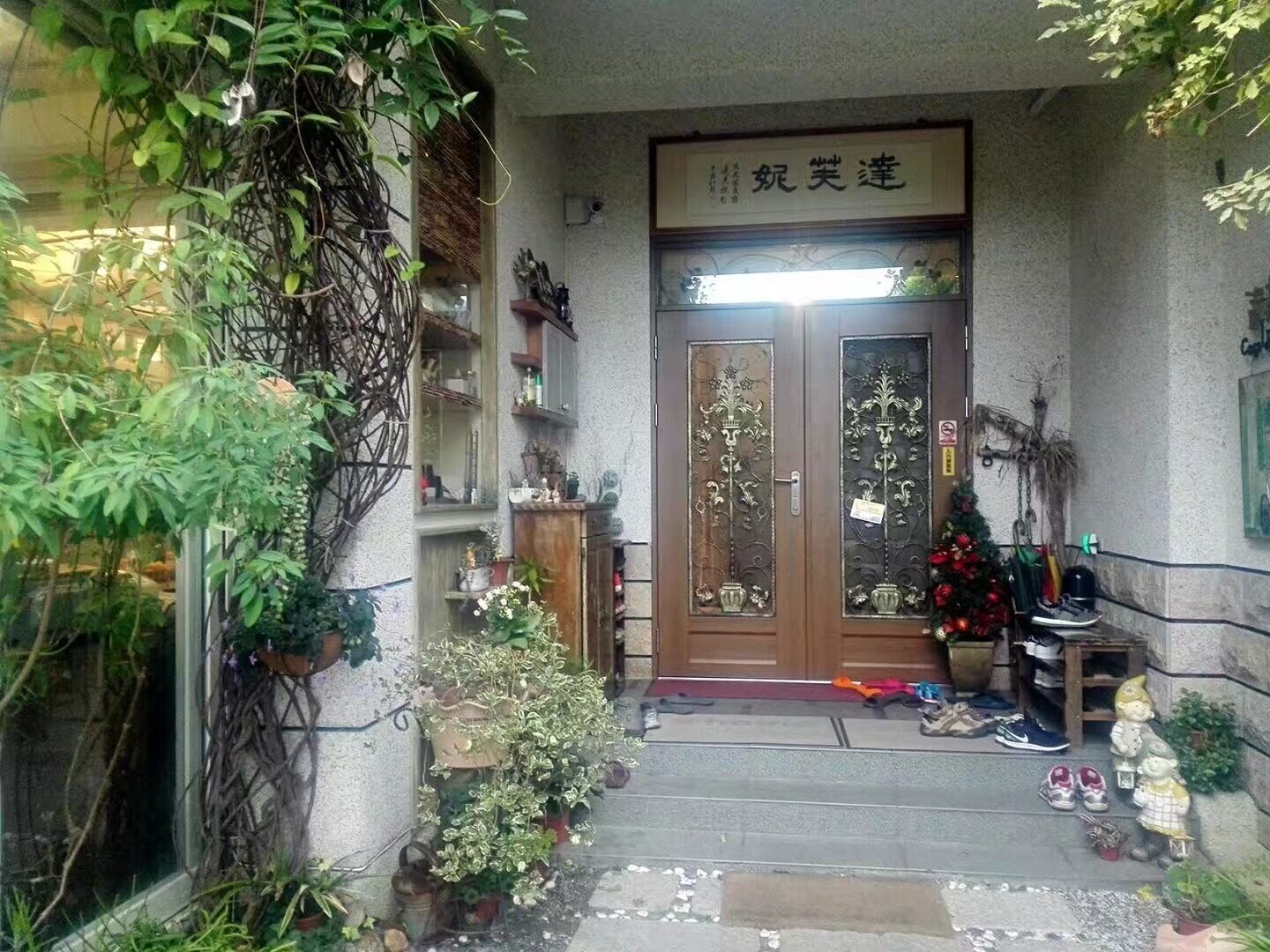 A traditional Japanese entrance with a wooden door, potted plants, and a small statue.