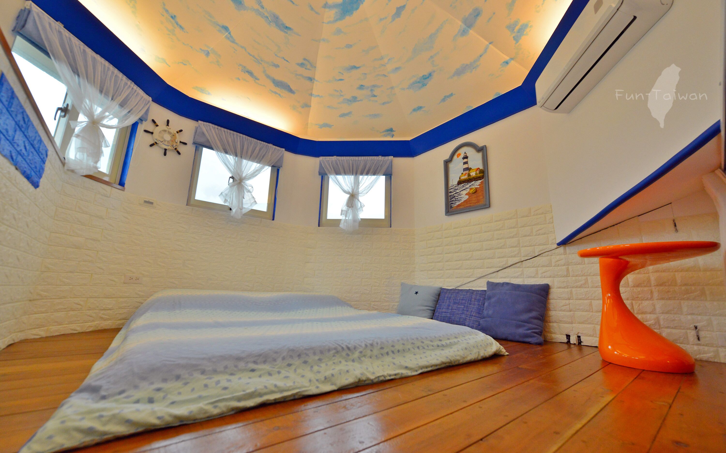 A room with a sloped ceiling, a bed with a striped blanket, a small table, and a wall clock.