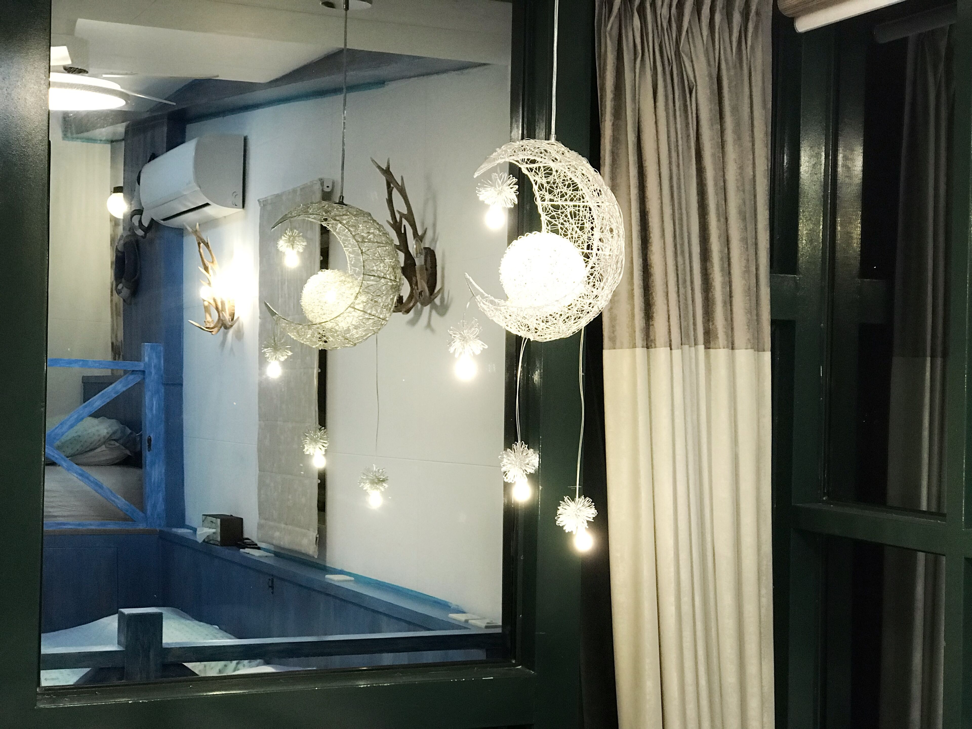 Una habitación con cama, ventana con cortinas e iluminación decorativa colgante.