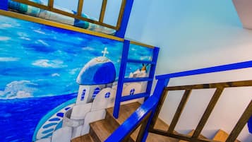 Escadaria com um mural de um edifício de cúpula azul e um navio, corrimãos de madeira e vista para o mar.