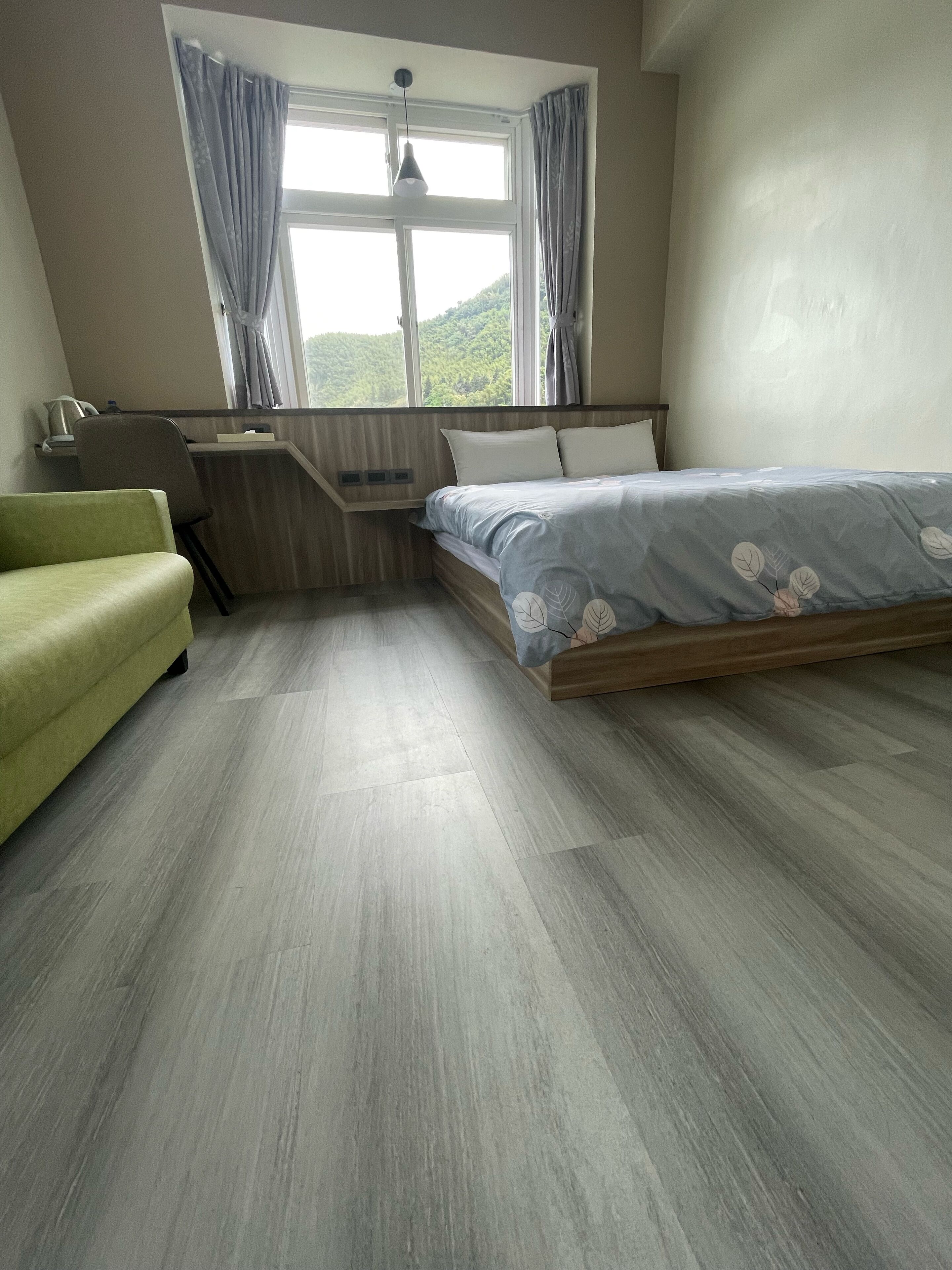 Un dormitorio con cama, escritorio y silla. Hay una ventana con cortinas y el suelo es de madera.