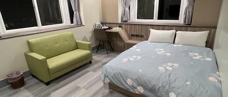 A hotel room with a bed, a green sofa, a desk, and two windows with curtains.