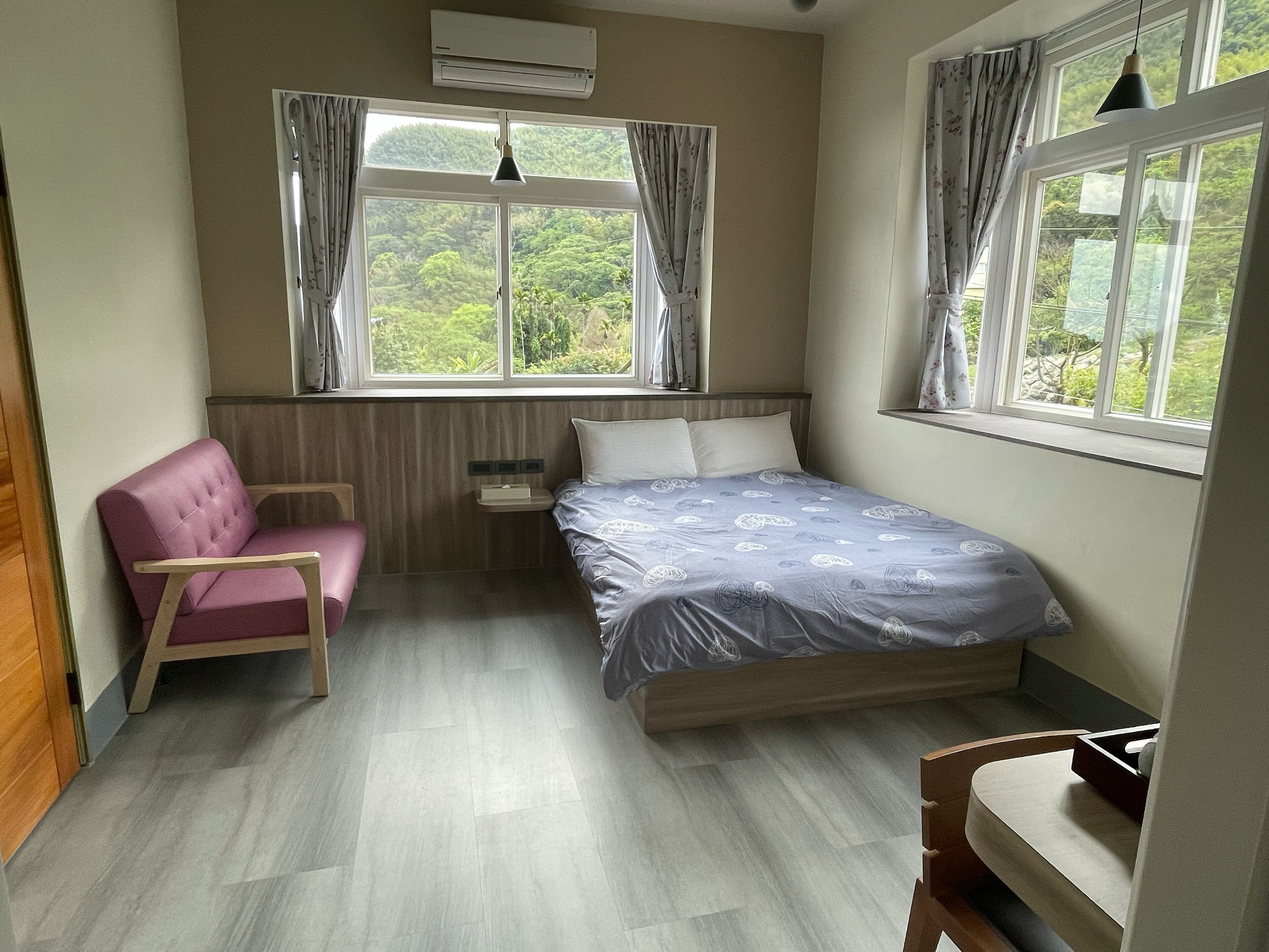 Une chambre à coucher avec un lit, une chaise, une table de chevet et une fenêtre avec des rideaux.