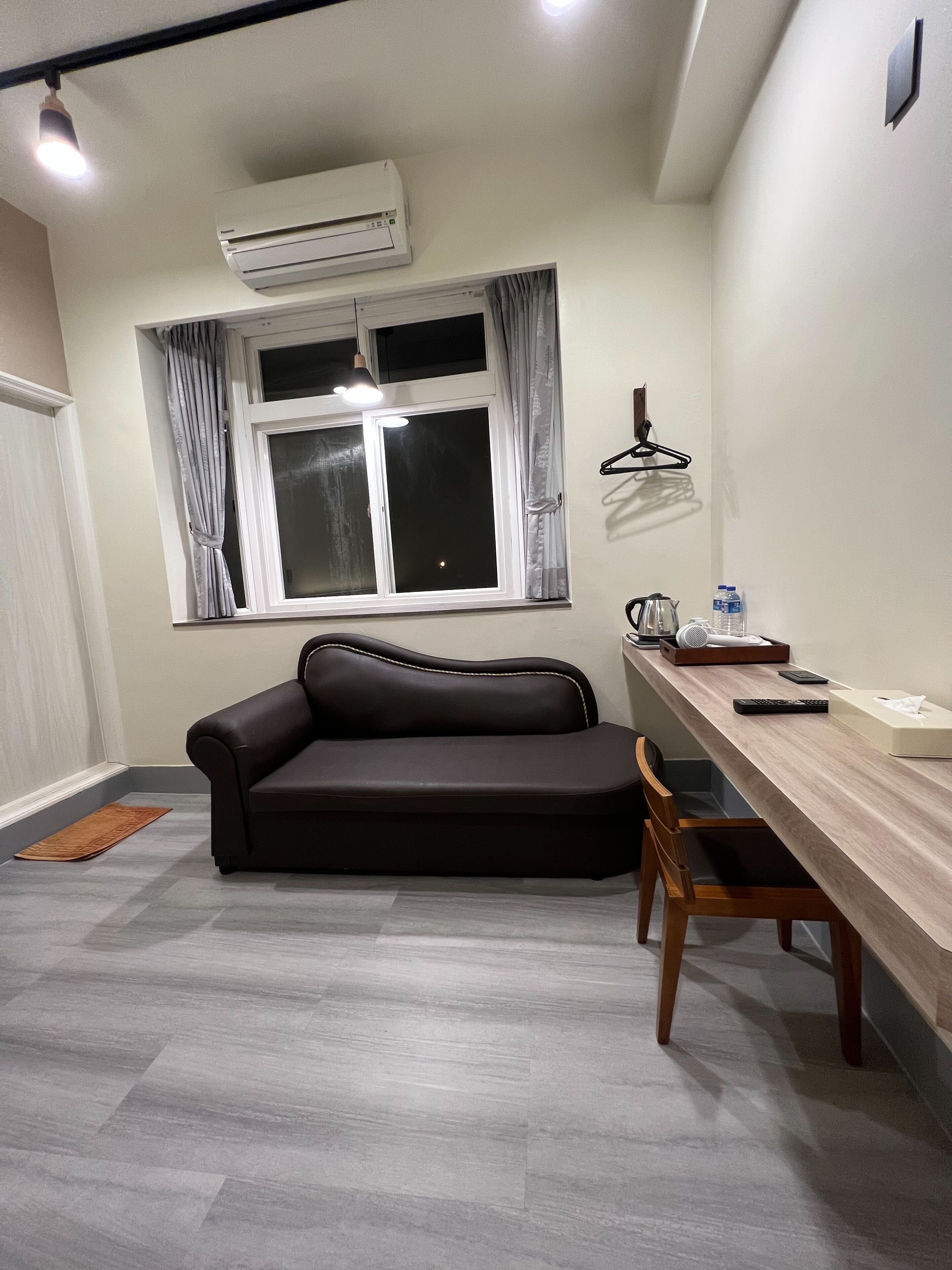 A modern living room with a black sofa, a wooden dining table, and a window with curtains.