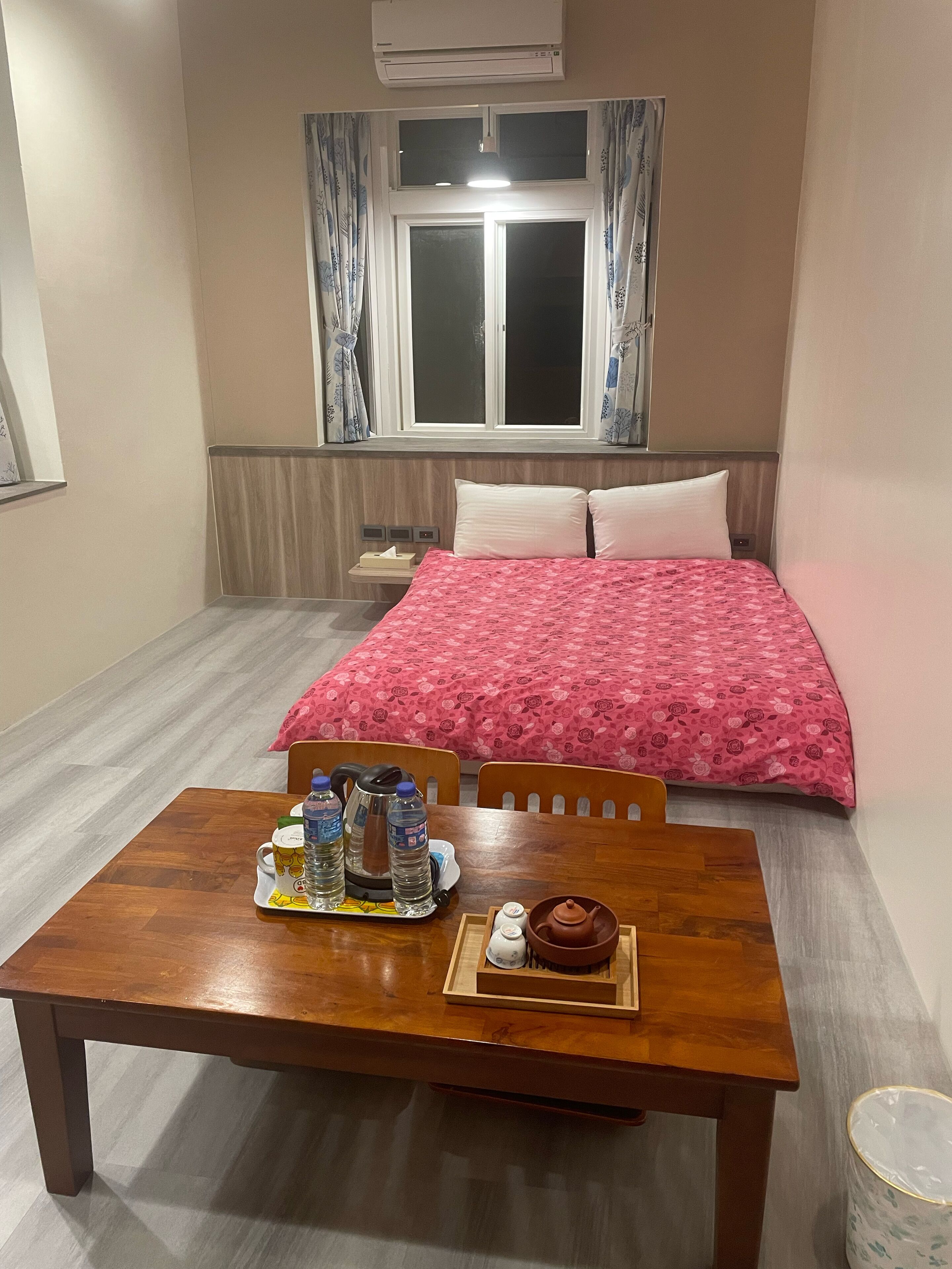Une chambre d’hôtel comprenant un lit, une table avec des articles pour le petit-déjeuner, une fenêtre avec des rideaux et un appareil de climatisation.