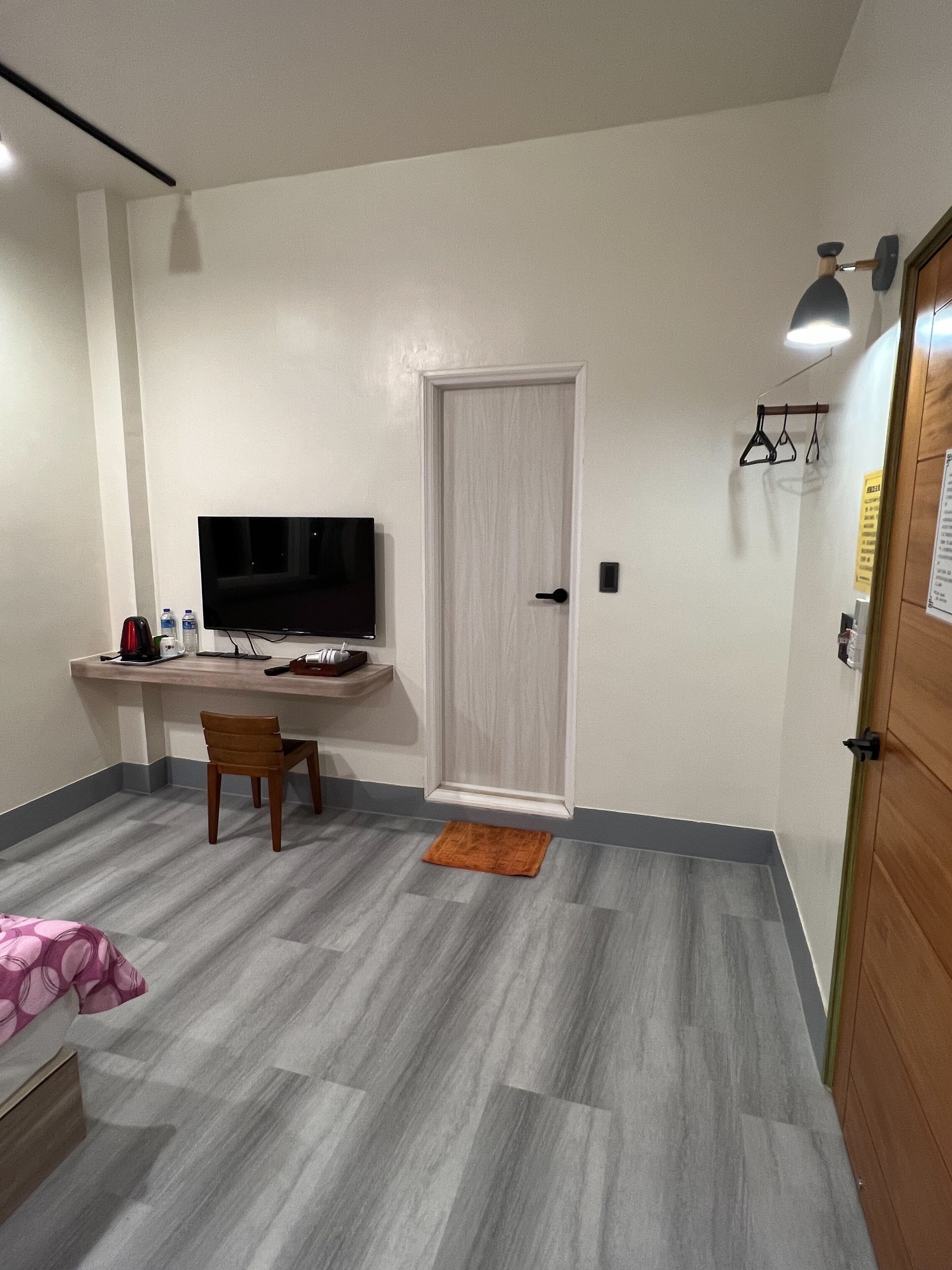 A small, modern room with a flat-screen TV, a wooden desk, a chair, and a small rug.