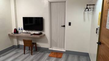 A small, modern room with a flat-screen TV, a wooden desk, a chair, and a small rug.