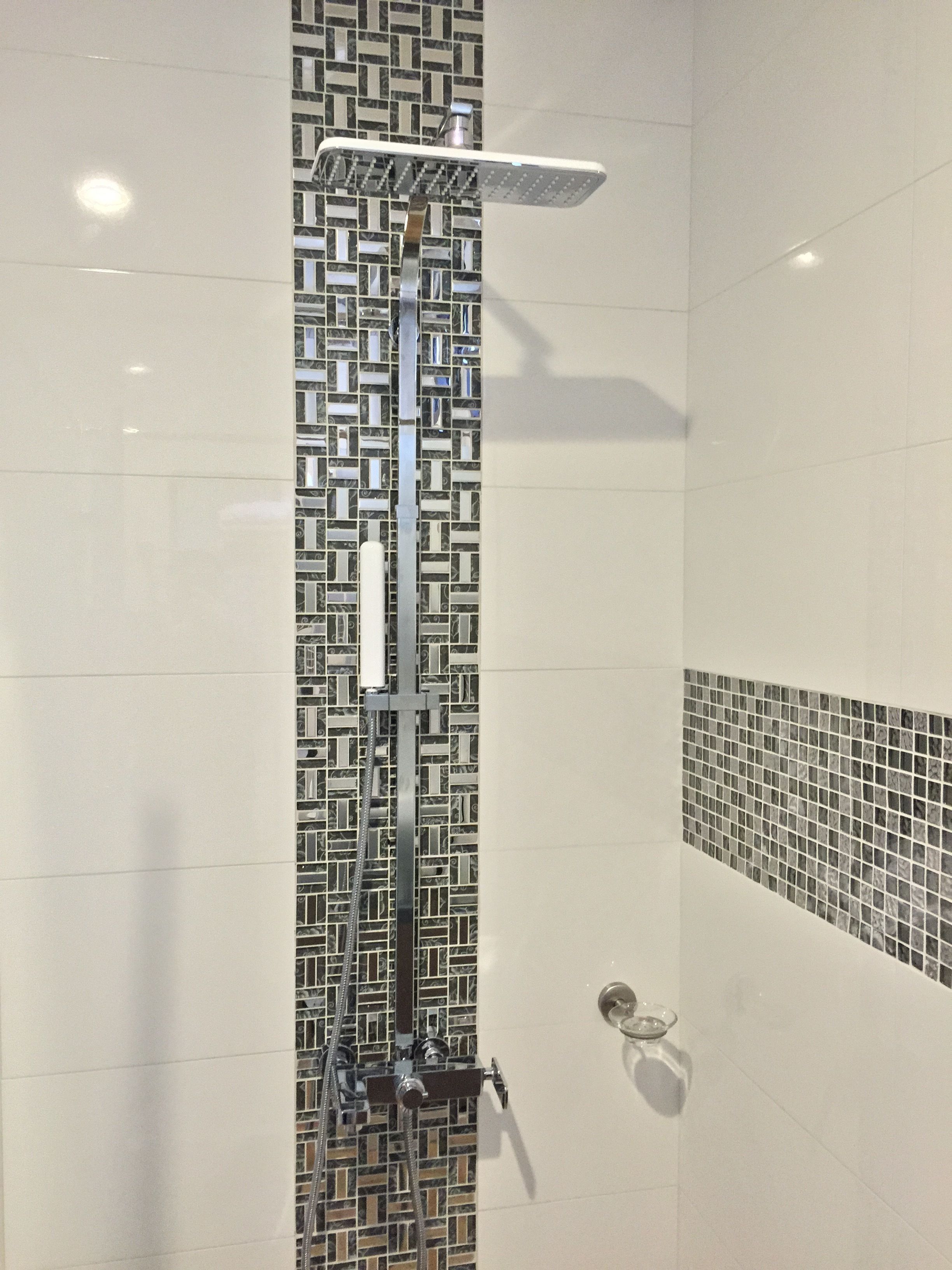 Ducha con detalles modernos y una salpicadura de azulejos geométricos, y cabezal de ducha con mampara de vidrio.