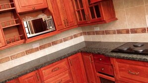 A kitchen with wooden cabinets, a microwave, and a stove. - Roma Gardens (Lusaka)