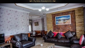 A living room with two leather sofas, a coffee table, a TV, and a painting on the wall. - Roma Gardens (Lusaka)