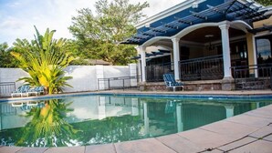 A swimming pool with lounge chairs, a covered patio area, and a large plant. - Roma Gardens (Lusaka)