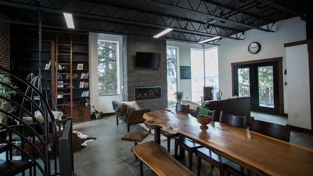 A spacious dining area with a long wooden table and benches, surrounded by bookshelves and a fireplace. - The Dwell House (Sugarcreek)