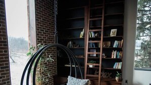 A modern room with a hanging chair, a brick wall, a bookshelf, and a large window. - The Dwell House (Sugarcreek)