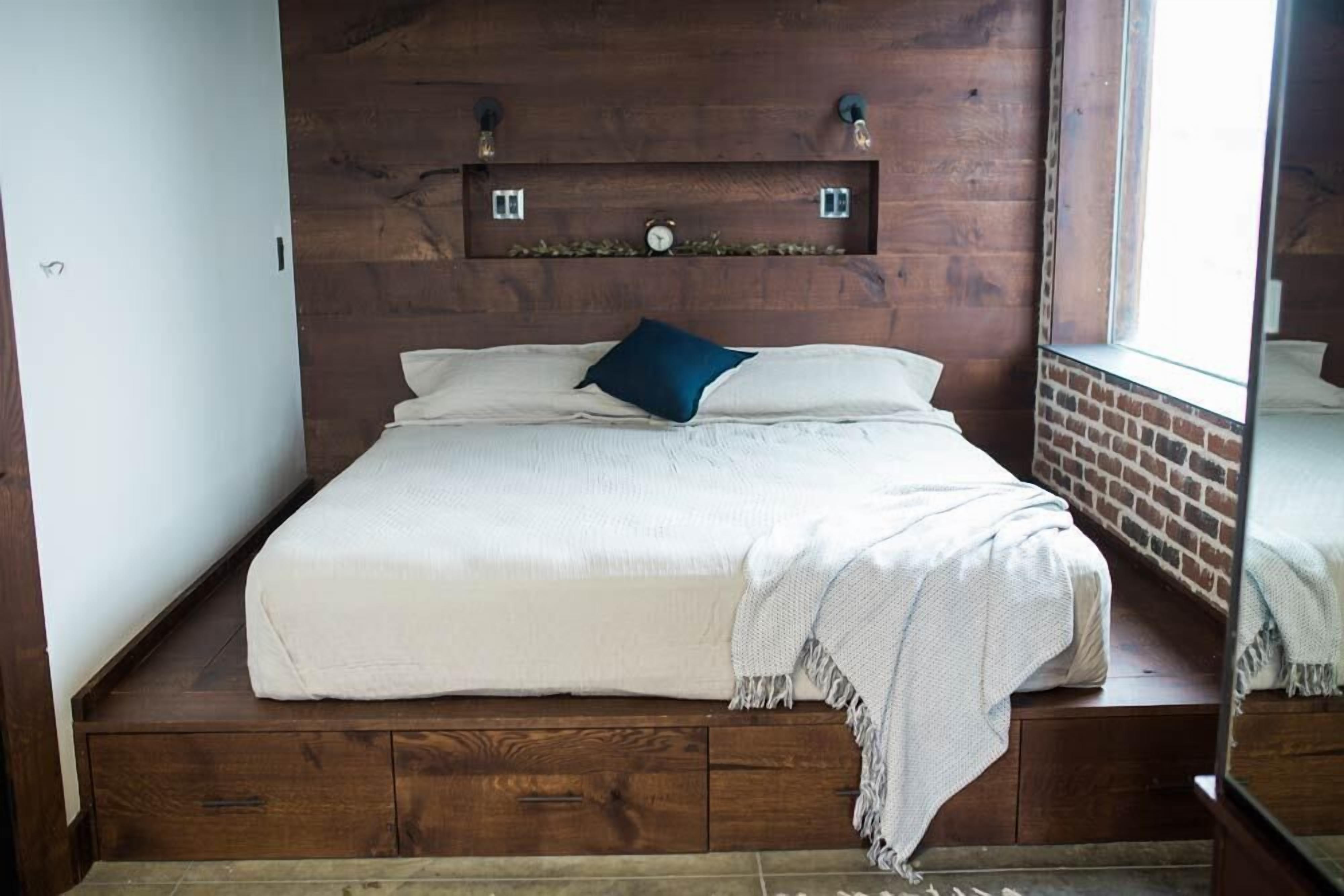 A bed with a wooden headboard, a small shelf above it, and a window to the right.