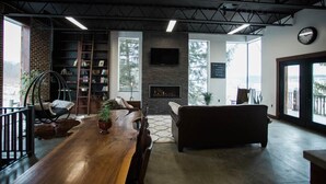 A spacious living area with a wooden dining table, a sofa, a fireplace, and a bookshelf. - The Dwell House (Sugarcreek)