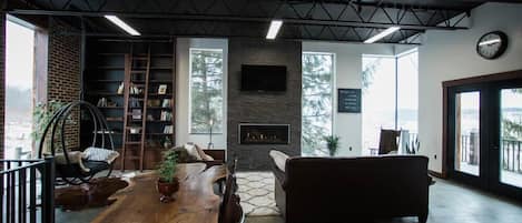 A spacious living area with a wooden dining table, a sofa, a fireplace, and a bookshelf.