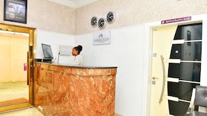 A reception desk with a marble finish, a digital screen, and a sign for Somerset Suites. There are clocks on the wall and a door labeled 'Restaurant/Bar'. - Somerset Suites (Lagos)