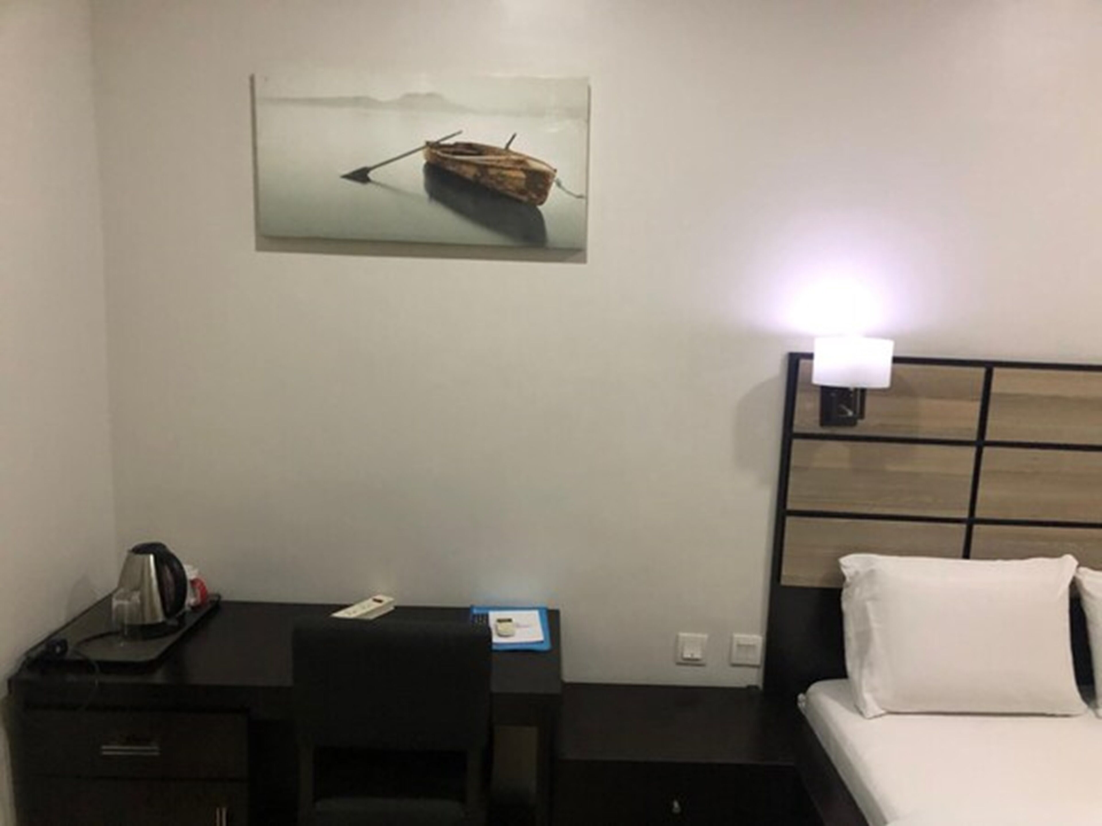 A hotel room with a bed, a desk, a chair, a coffee maker, and a painting of a boat on the wall.