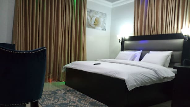 A hotel room with a bed, a chair, and a nightstand. - Somerset Suites (Lagos)