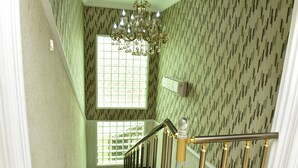 A staircase with a chandelier, patterned wallpaper, and a window with a grid design. - Somerset Suites (Lagos)