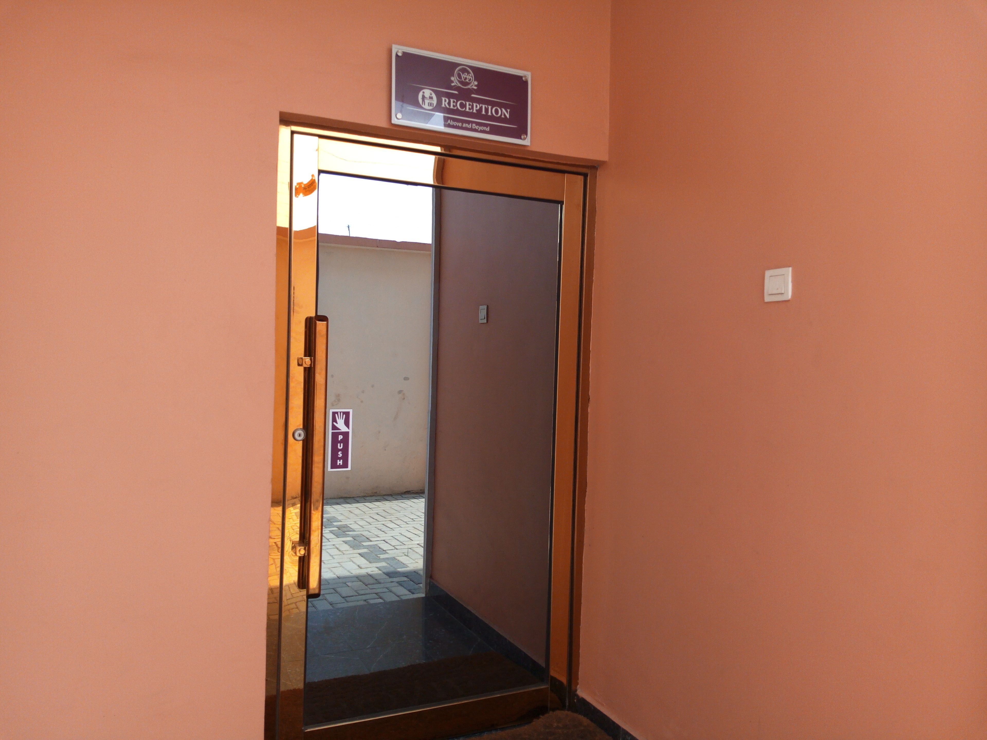 A reception area with a sign above a door, a push button on the door, and a tiled floor.