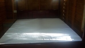 A room with a large bed, wooden walls, and a small window.