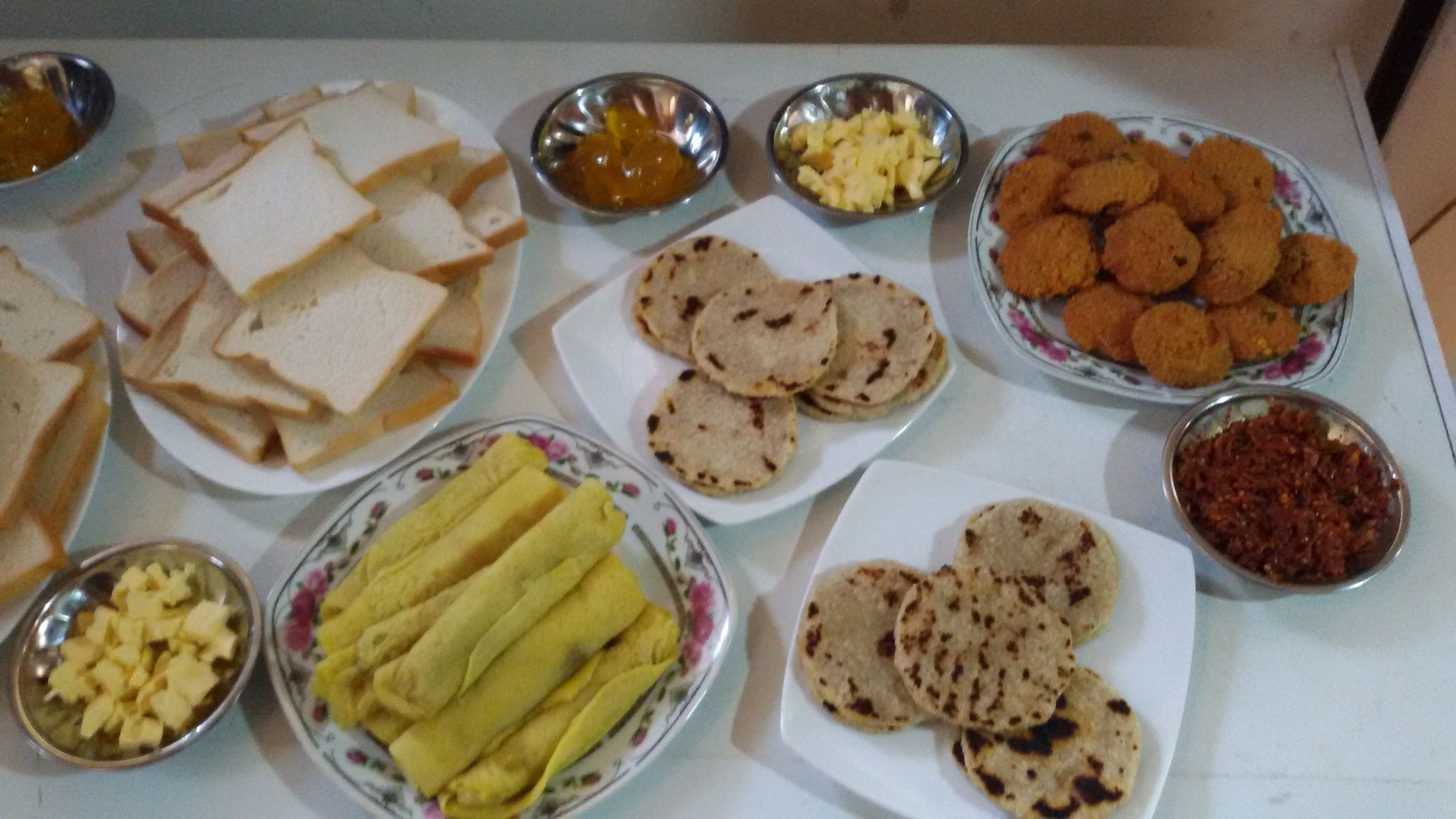 Uma mesa com diversos alimentos, incluindo pão, pães sírios e um prato com fatias amarelas.