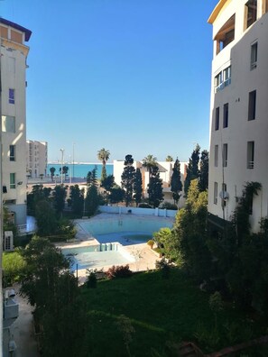 A residential building with a swimming pool, surrounded by greenery and overlooking a body of water. - Furnished Appartement Malabata Beach (Tangier)