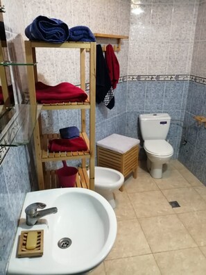 A bathroom with a white sink, a toilet, a glass shelf with towels, and a wooden shelf with folded towels. - Furnished Appartement Malabata Beach (Tangier)